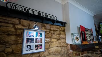 A wall with a 'Welcome to the Mad House' sign, a framed photo collage, and a dartboard.
