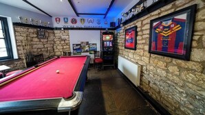 A billiards room with a red pool table, a dartboard, and a framed sports jersey on the wall. - The Oddfellows Arms (Leeds)