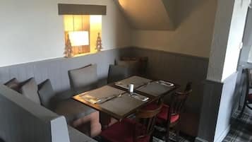 A cozy corner with a wooden table set for two, a cushioned bench, and a small window with a lamp.