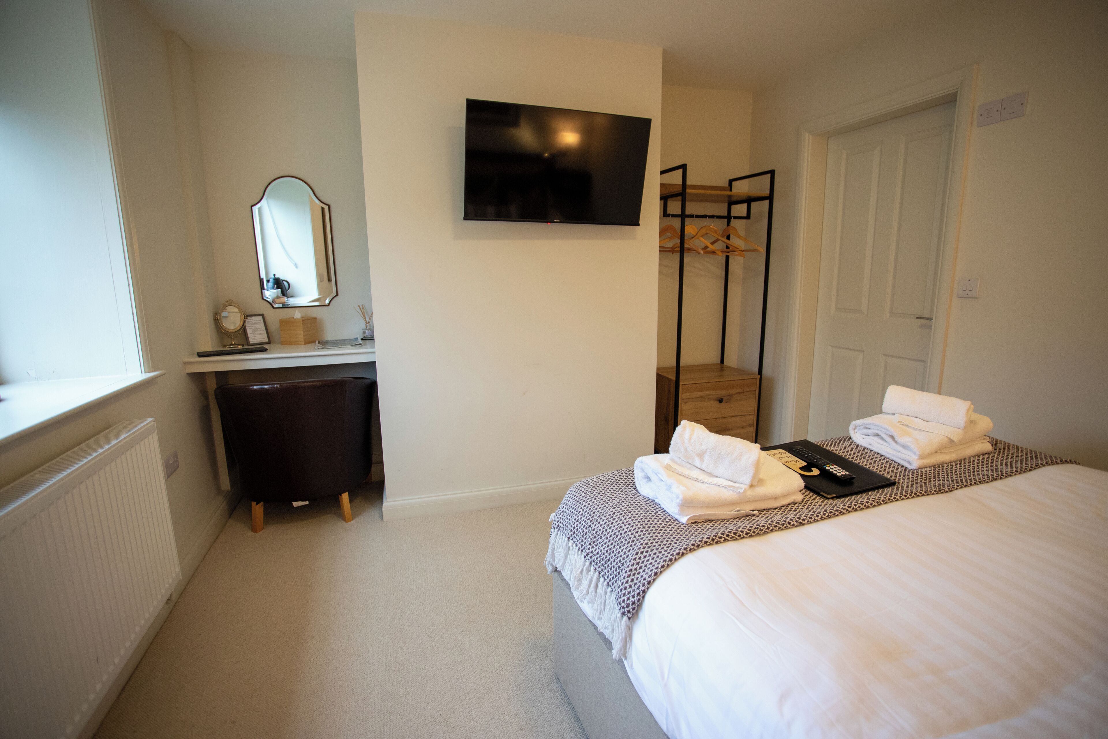 Une chambre d’hôtel équipée d’un lit, d’une télévision, d’un miroir, d’une commode et d’un porte-manteau.