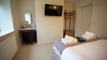 Une chambre d’hôtel équipée d’un lit, d’une télévision, d’un miroir, d’une commode et d’un porte-manteau.