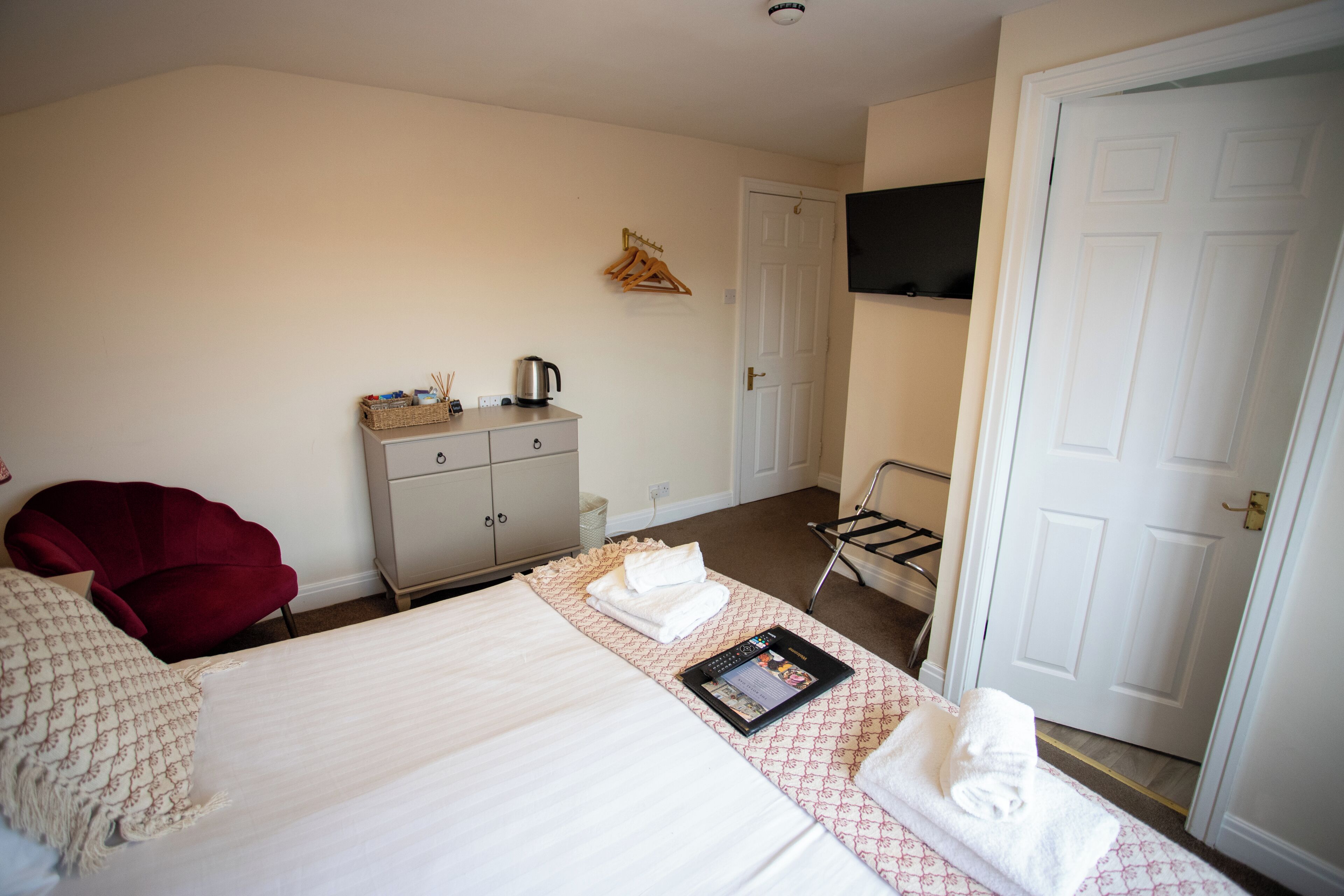 A hotel room with a bed, a desk, a chair, a TV mounted on the wall, and a door.