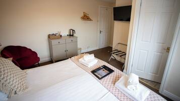A hotel room with a bed, a desk, a chair, a TV mounted on the wall, and a door.
