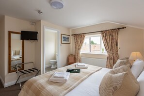 Ein Hotelzimmer mit Bett, Wand-Fernseher, Fenster mit Vorhängen, Heizkörper und kleinem Tisch mit Handtüchern.