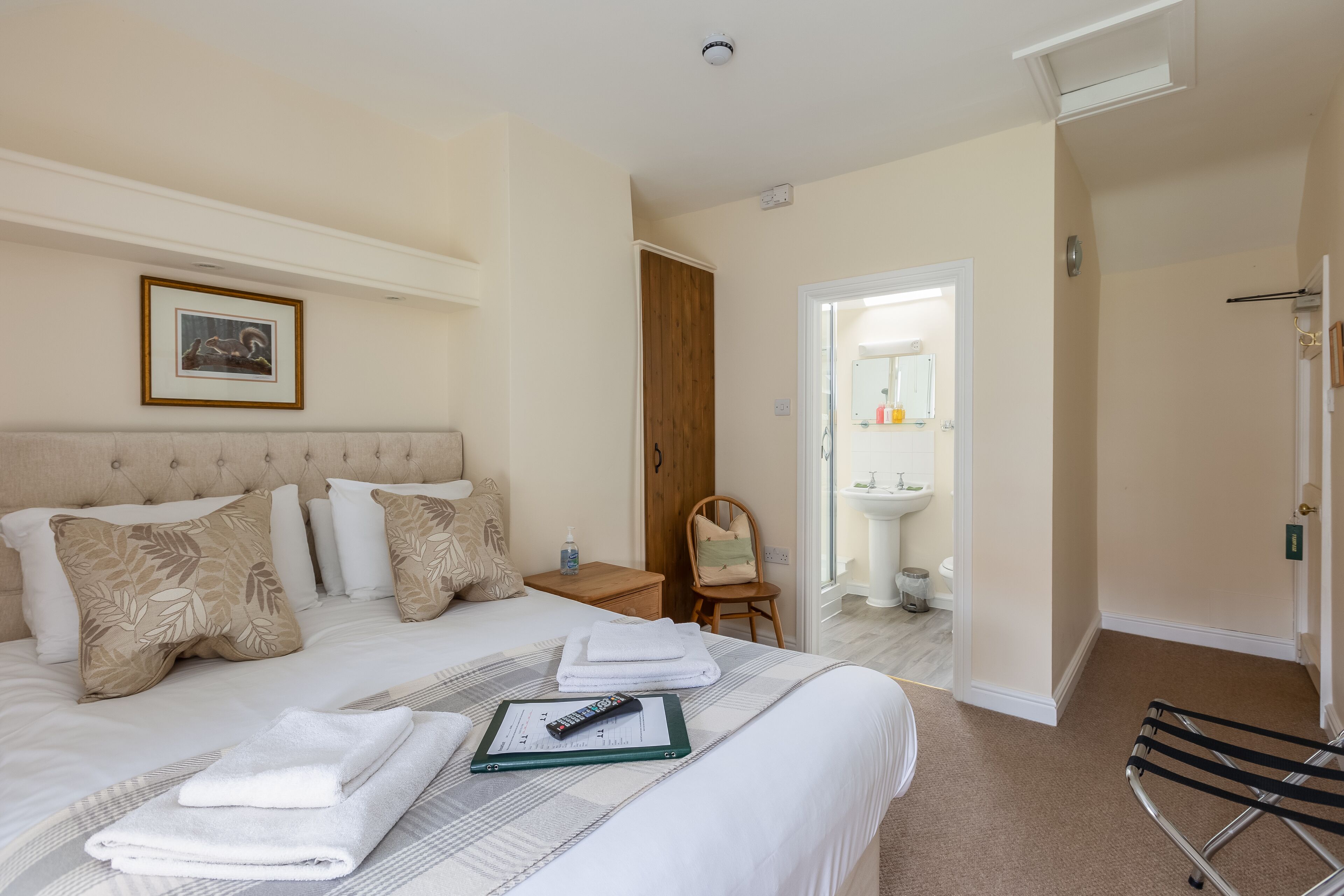 A hotel room with a large bed, a bedside table with a remote control, and a chair.