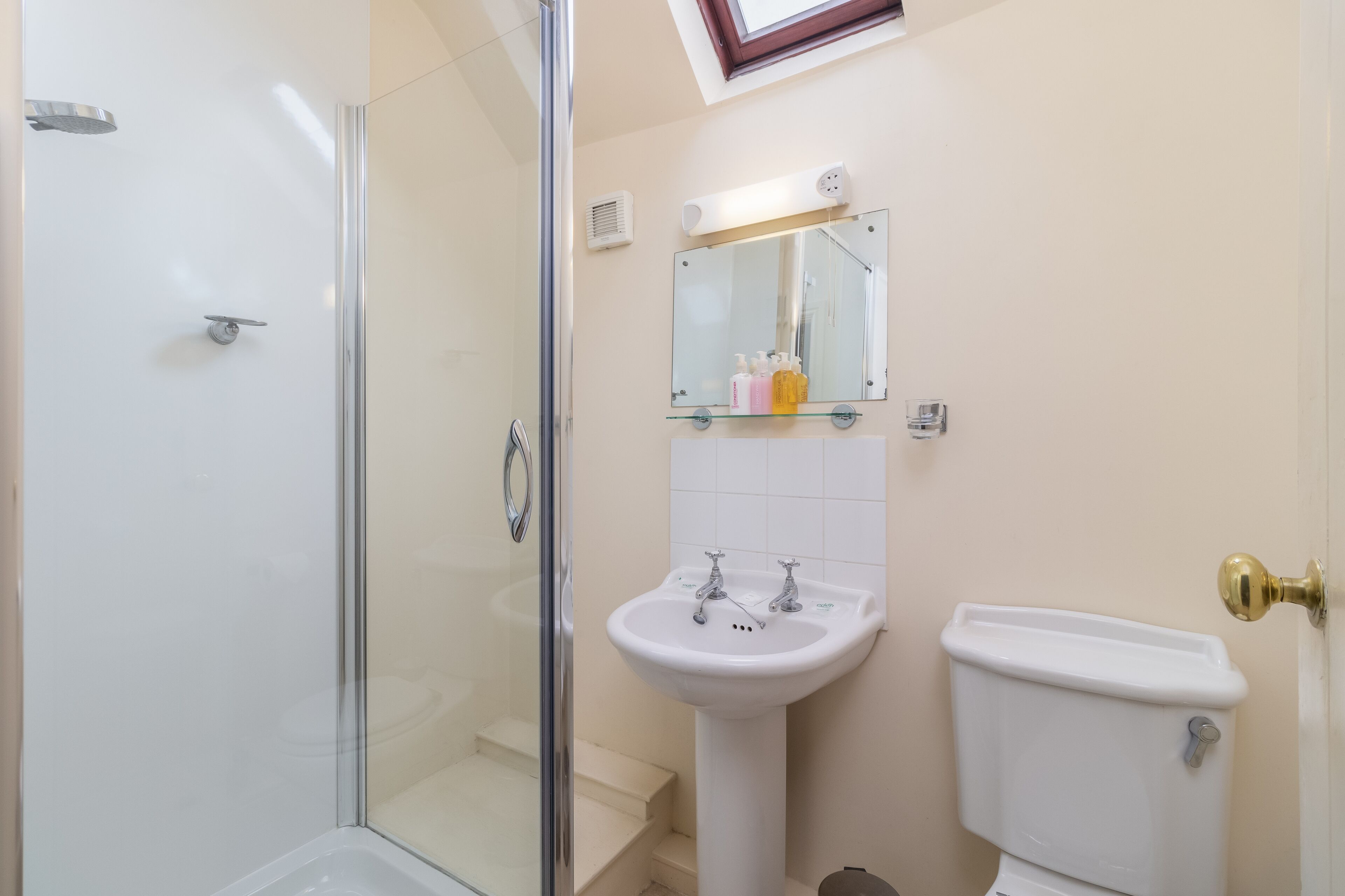 A bathroom with a glass shower enclosure, a pedestal sink, and a toilet.