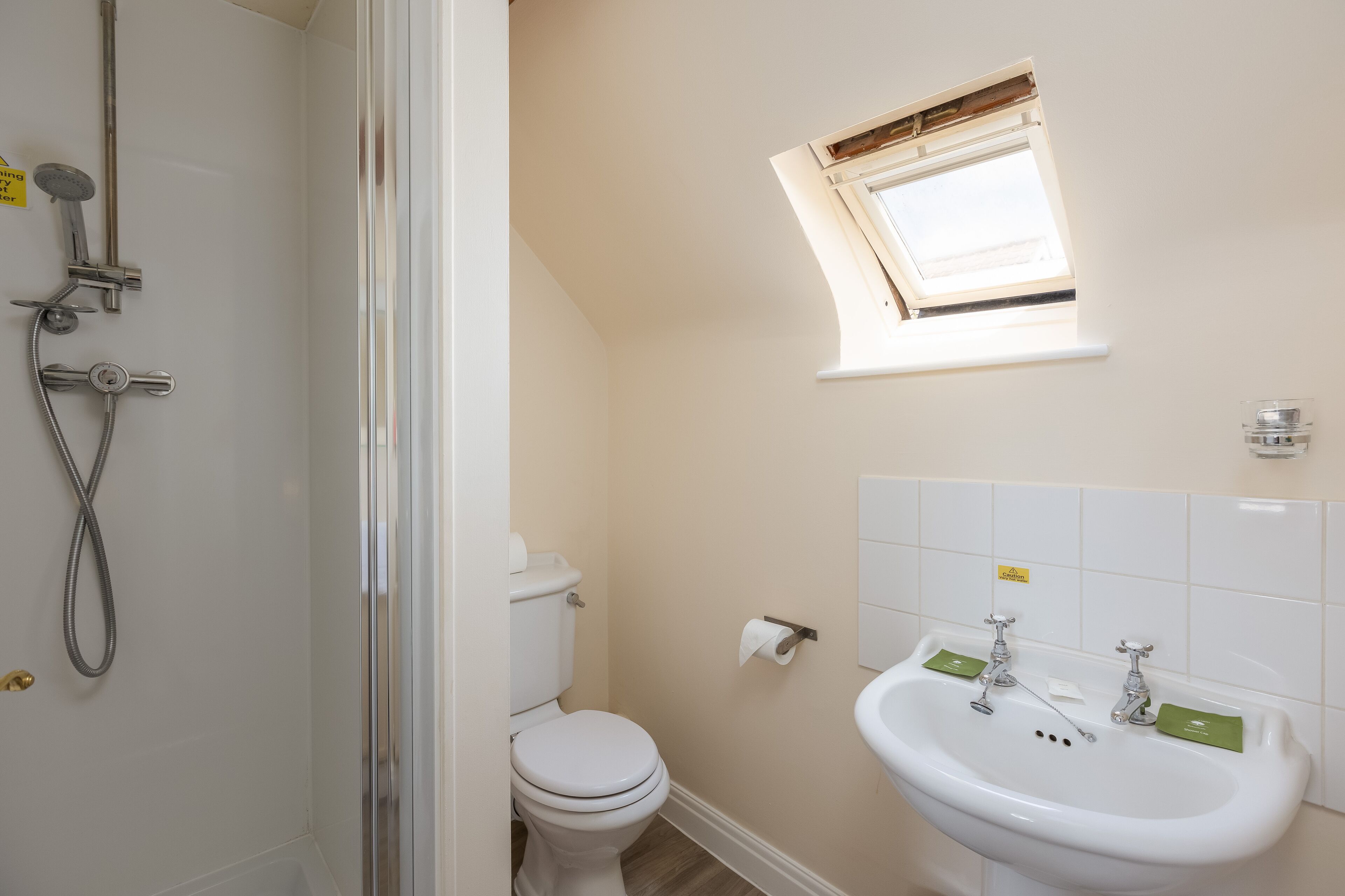 Et badeværelse med brusebad, toilet, håndvask og et lille vindue.