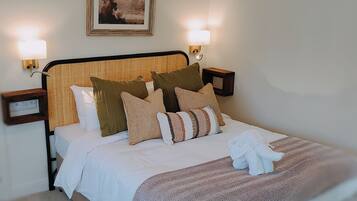 Una cama bien hecha con un plaid estampado, un cabecero con textura tejida y dos lámparas fijadas a la pared.