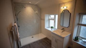 A bathroom with a glass-enclosed shower, a sink with a mirror above it, and a window with blinds.
