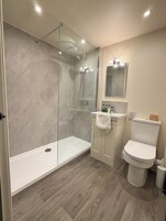 Un baño moderno con ducha envuelta en vidrio, inodoro blanco y lavamanos con espejo arriba.
