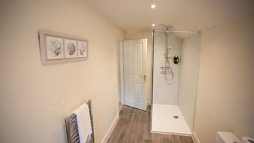 Un baño moderno con cabina de ducha de vidrio, piso de madera y puerta blanca.