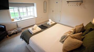 A hotel room with a bed, a window, a door, a radiator, and a television.