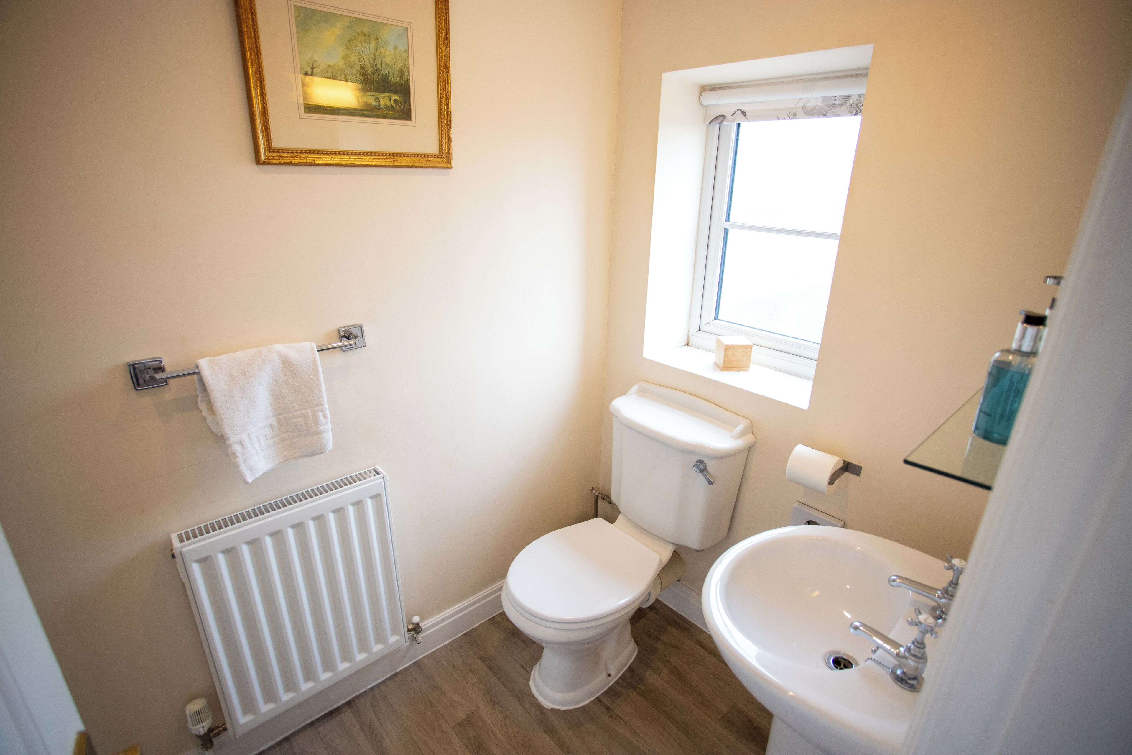 Ein Badezimmer mit Toilette, Waschbecken, Heizkörper, Handtuchhalter und einem Fenster.