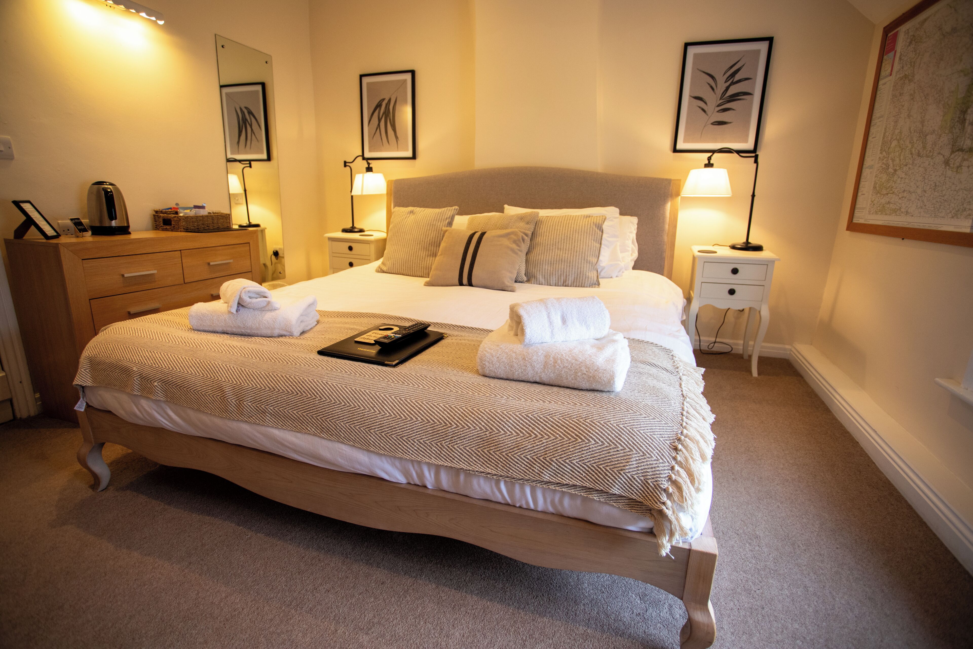 A neatly made bed with a patterned bedspread, two bedside lamps, a wooden dresser, and a framed picture on the wall.
