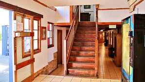 A hallway with a wooden staircase, a vending machine, and a sign indicating emergency use sliding doors. - Brisbane Manor Hotel (Fortitude Valley)