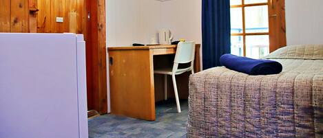 Una habitación con escritorio de madera, una silla, una cama con colcha estampada y una ventana con cortinas azules.