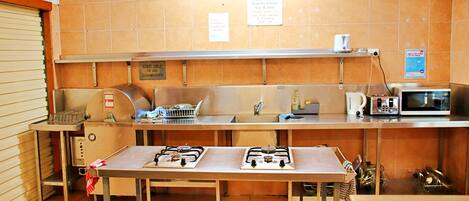 A kitchen with stainless steel appliances, including a stove, microwave, and sink. There are signs on the wall and a tiled backsplash.