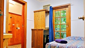 A bedroom with a bed, a wooden wardrobe, a small kitchenette, and a window with a view of greenery. - Brisbane Manor Hotel (Fortitude Valley)