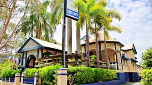 A hotel with a tropical theme, featuring a large signboard, a wooden fence, and lush greenery. - Brisbane Manor Hotel (Fortitude Valley)