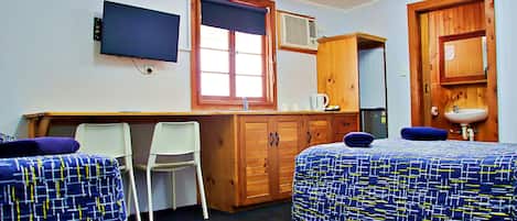 A room with two beds, a desk, a chair, a television, and a window.