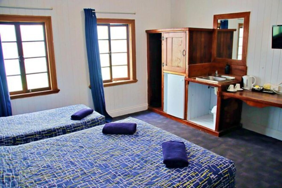 A room with two beds, a wooden desk, a mirror, and a window with curtains.
