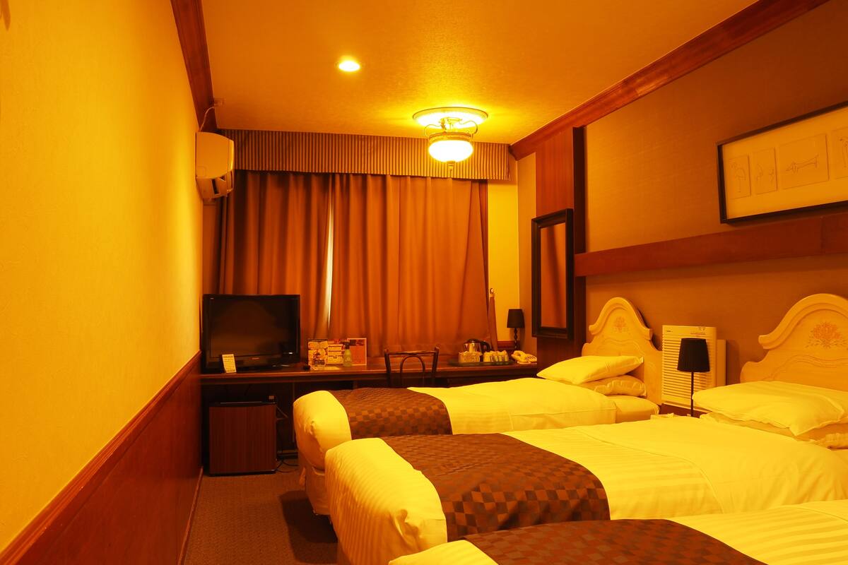 A hotel room with two beds, a desk with a television, a mirror, and a nightstand with a lamp.