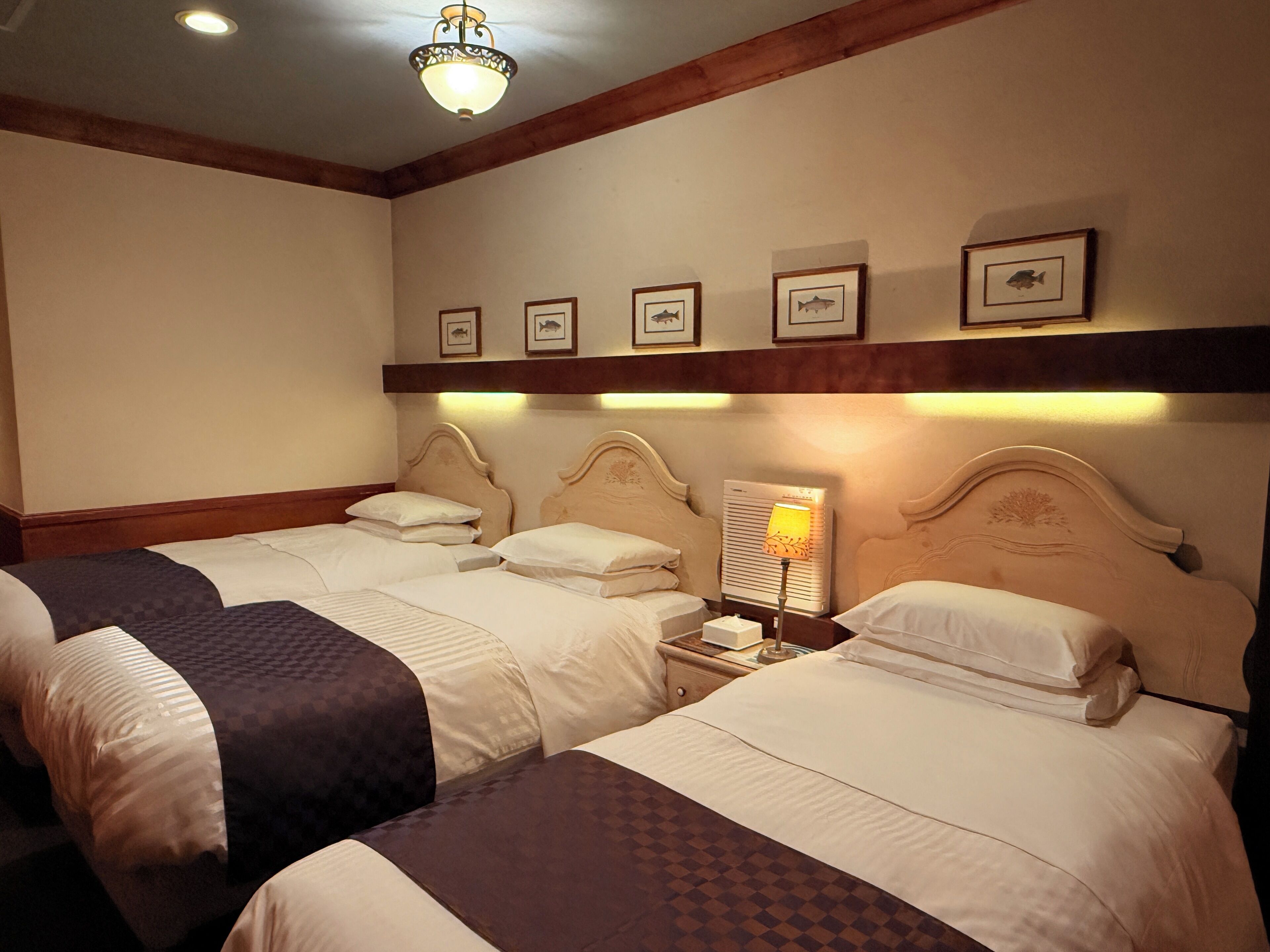A hotel room with two beds, a nightstand with a lamp, and framed pictures on the wall.