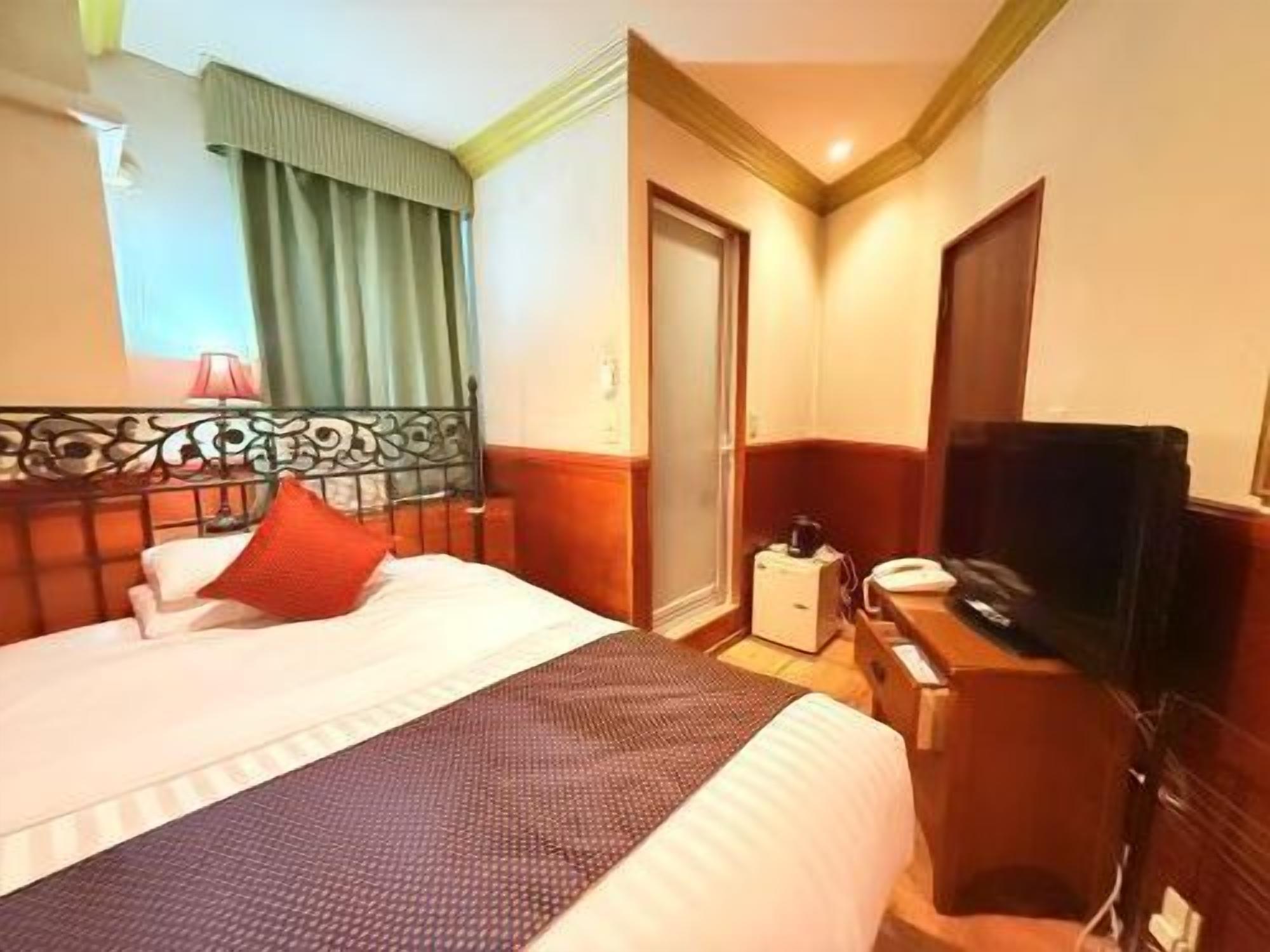 A hotel room with a bed, a TV, a desk, and a door.