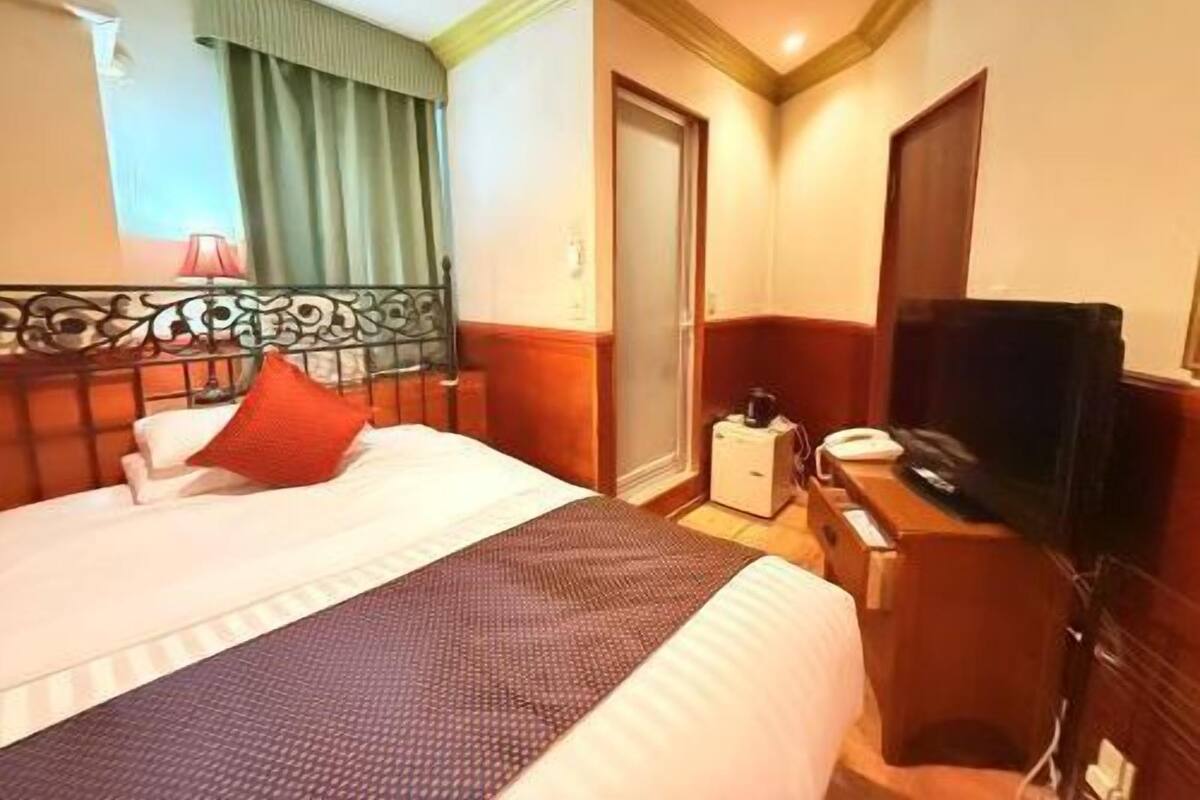 A hotel room with a bed, a TV, a desk, and a door.