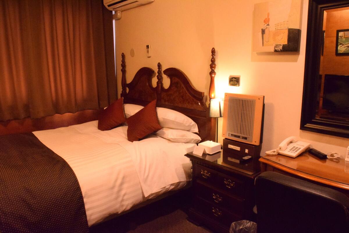 A hotel room with a large bed, a bedside table with a lamp, a telephone, and a mirror.