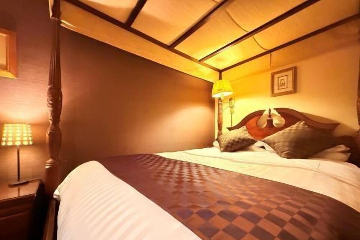 A hotel room with a bed, a nightstand, a lamp, and a picture on the wall.