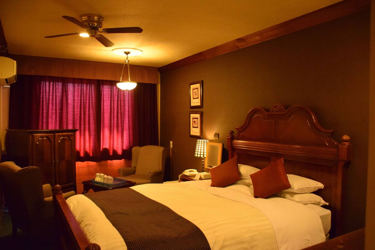 A hotel room with a bed, a desk, a chair, a ceiling fan, and a window with curtains.