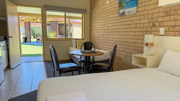 A hotel room with a bed, a dining table, chairs, a TV, and a view of the outside.