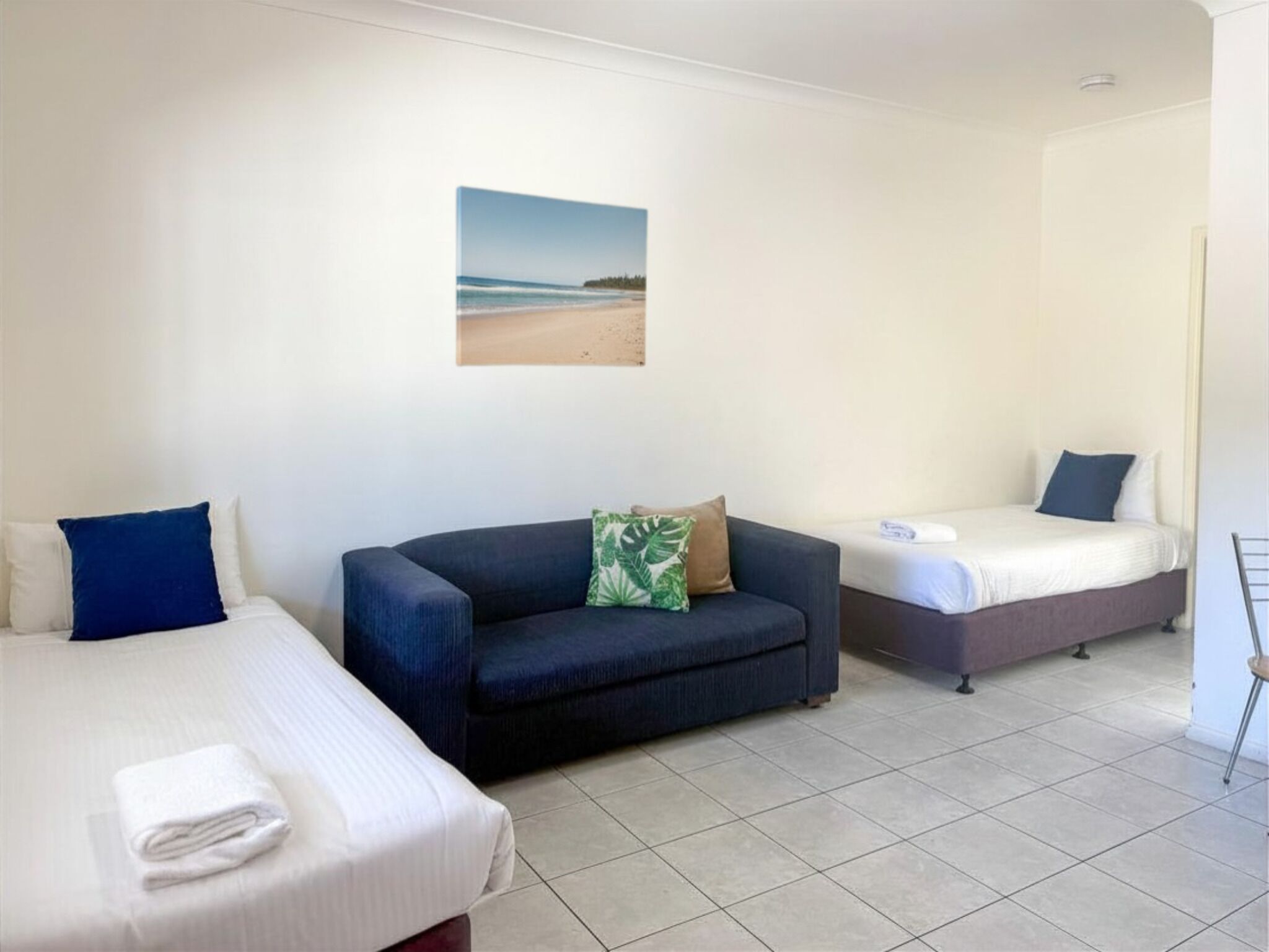 A hotel room with two beds, a sofa, and a wall-mounted picture.