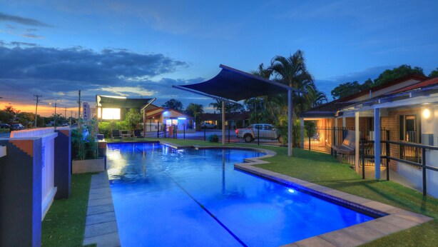 A swimming pool with a covered area, surrounded by a fence, and adjacent to a building with a visible entrance.