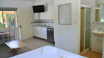 Hotelkamer met een bed, een tafeltje, een stoel, een kitchenette, een douche en een televisie.