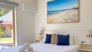 Ein Hotelzimmer mit Bett, einem Gemälde mit Strandblick, Deckenventilator und Fenster mit Klimaanlage.