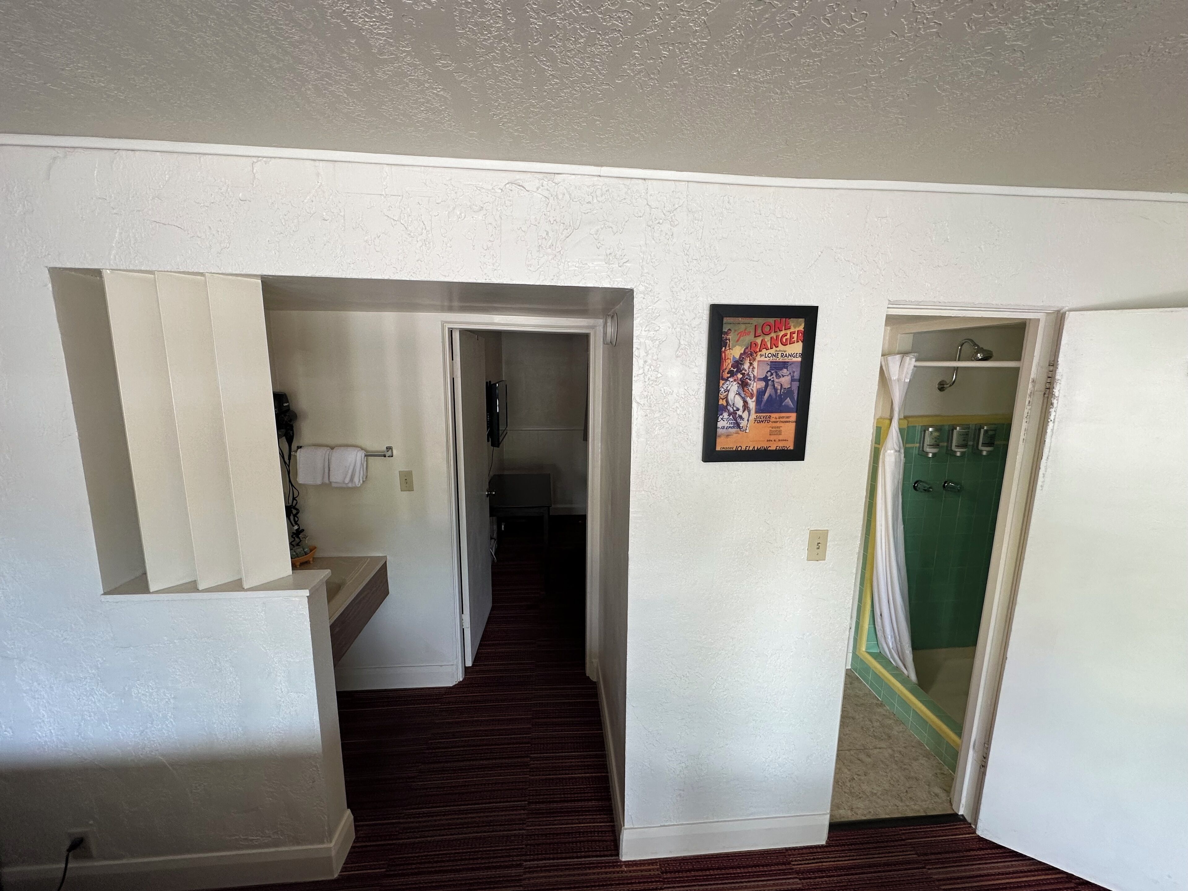 A hallway with a bathroom on the right, a door leading to another room, and a framed movie poster on the wall.