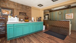 Een keuken met blauwgroene kastjes, een houten vloer, een magnetron, een koffiezetapparaat en een klok aan de muur.