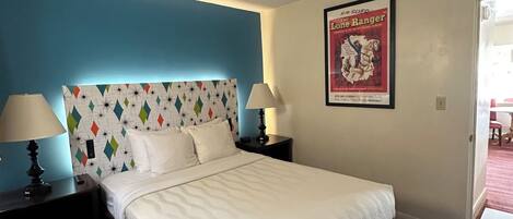 A hotel room with a bed, two bedside tables with lamps, a poster on the wall, and a door leading to another room.