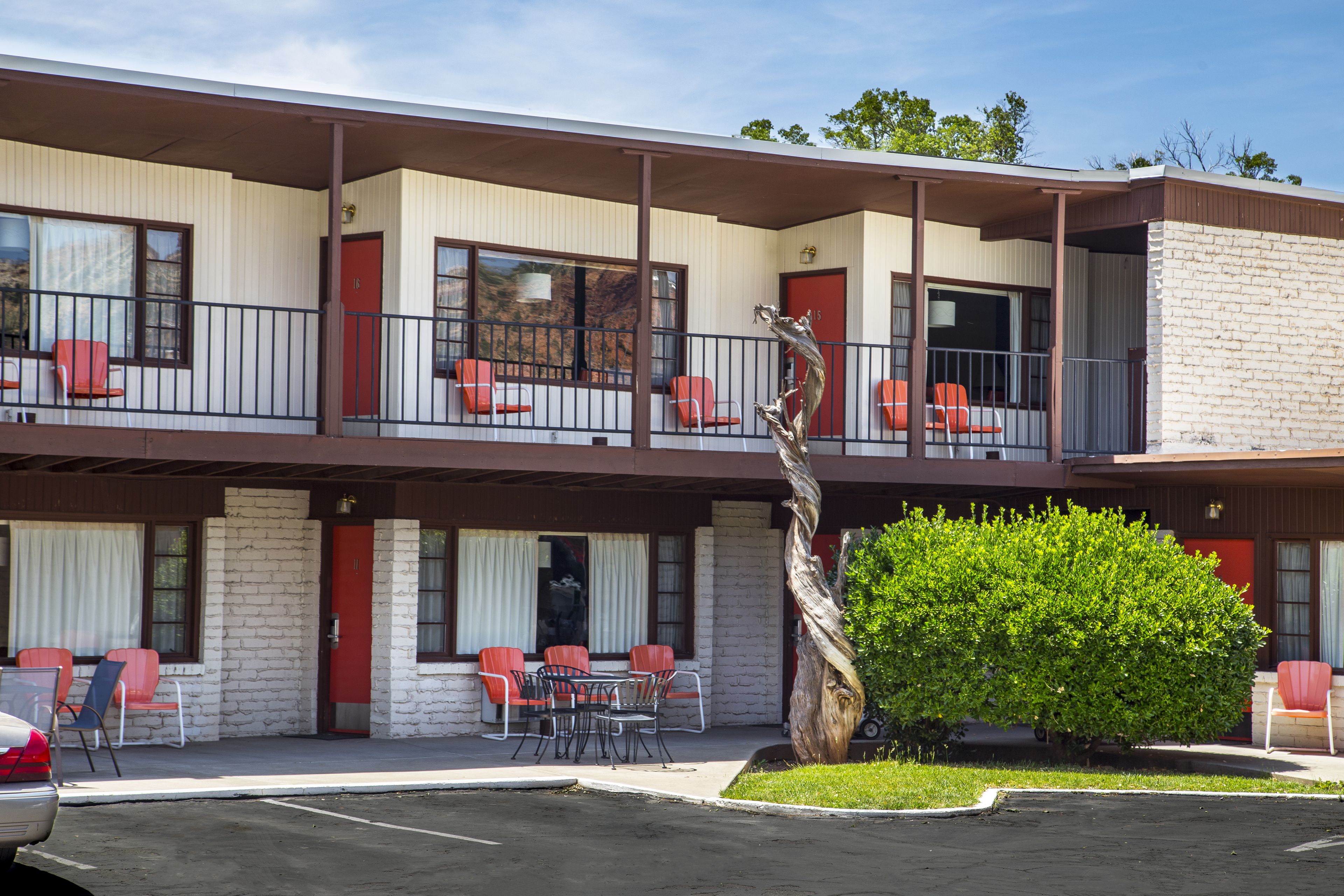 Un motel avec un bâtiment à deux étages, de nombreuses chambres avec des portes rouges et un parking.