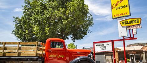 Un camión rojo antiguo estacionado frente a Aikens Lodge, con un gran árbol y un cartel de bienvenida.
