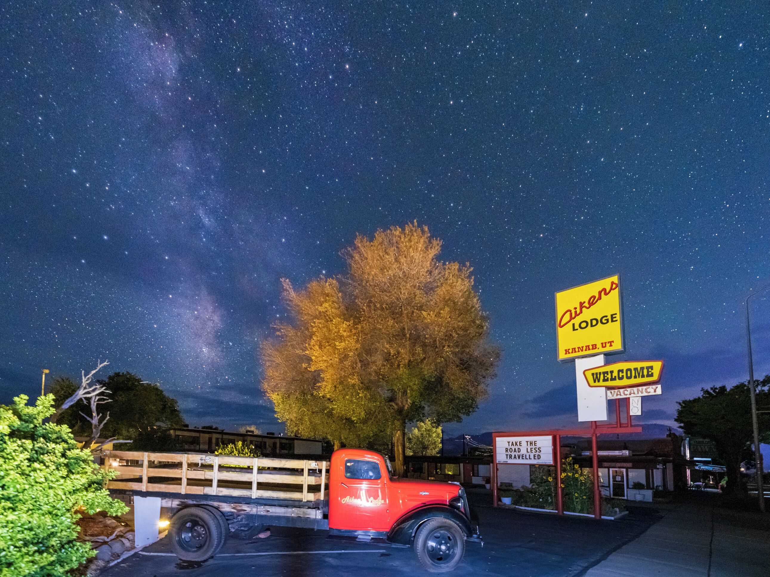 A red truck parked in front of a motel with a 'Welcome' sign and a 'Vacancy' sign.