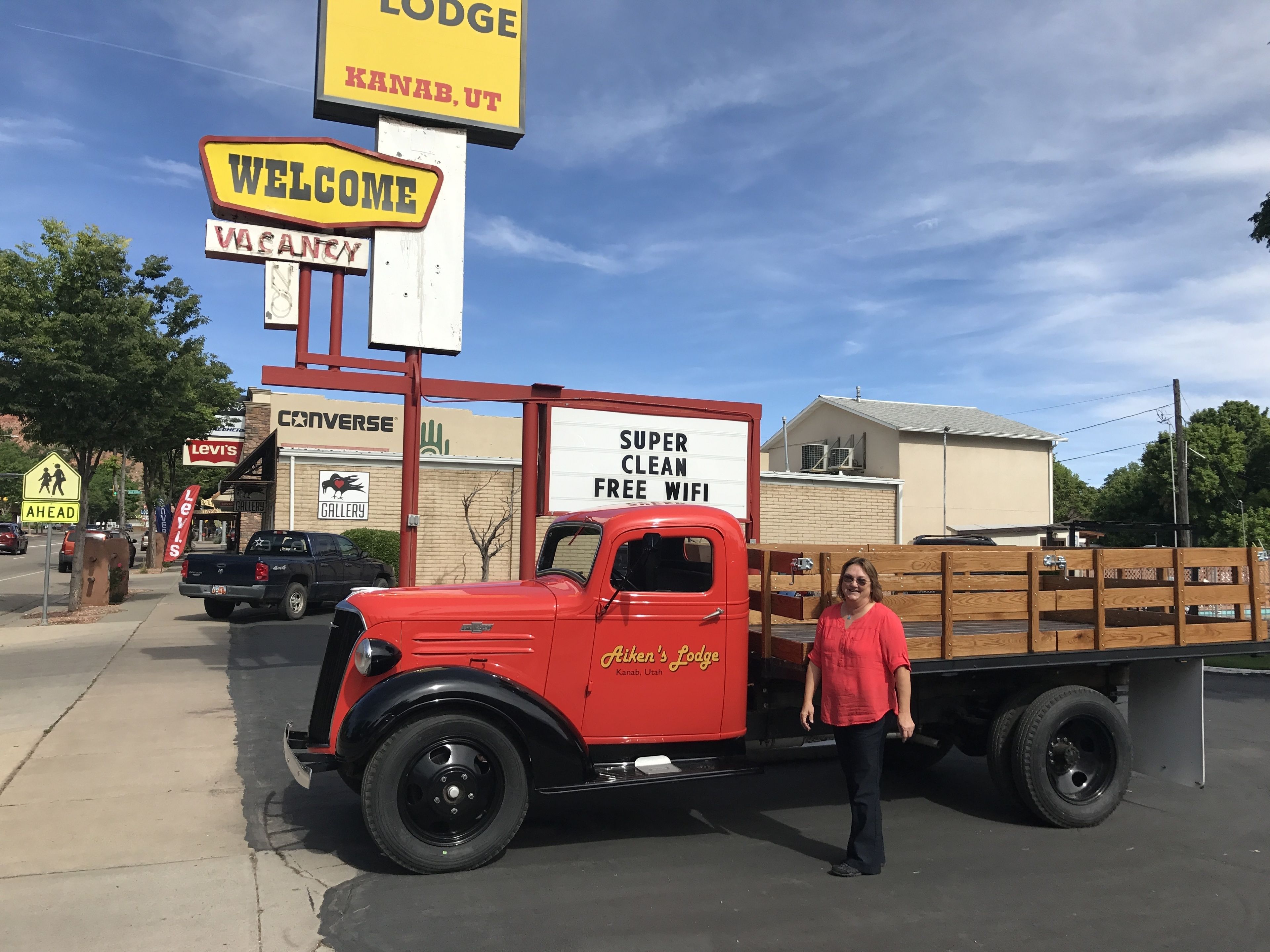 A vintage red truck parked in front of a motel with a 'Welcome' sign and a 'Vacancy' sign.
