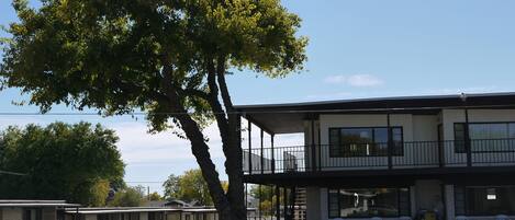 A motel with a two-story building, a covered outdoor seating area, and a large tree in front.