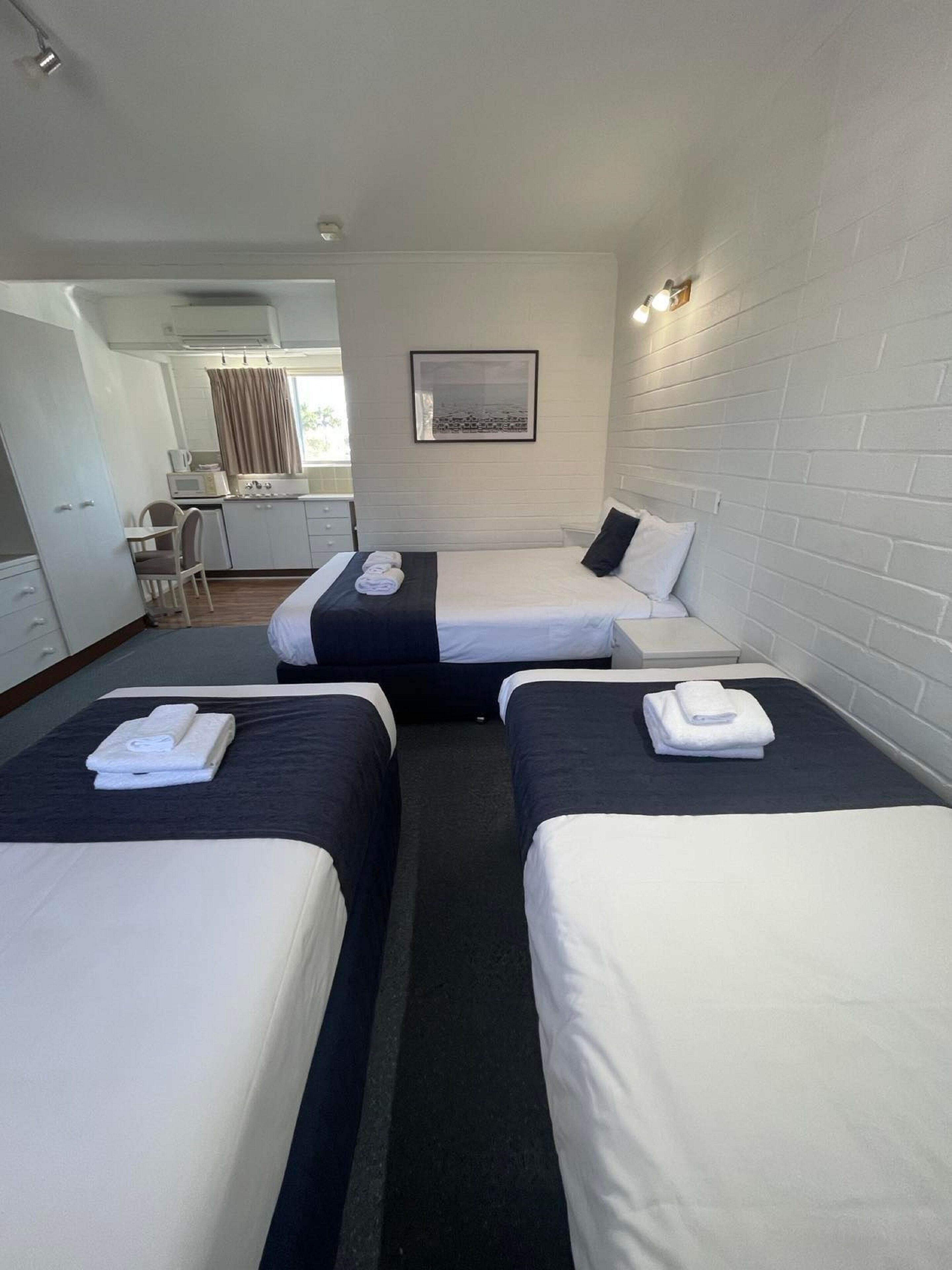 A hotel room with two beds, a kitchenette, a dining area, and a bathroom.