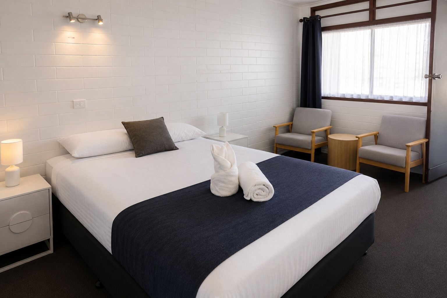 A hotel room with a large bed, two armchairs, a small table, and a window with curtains.
