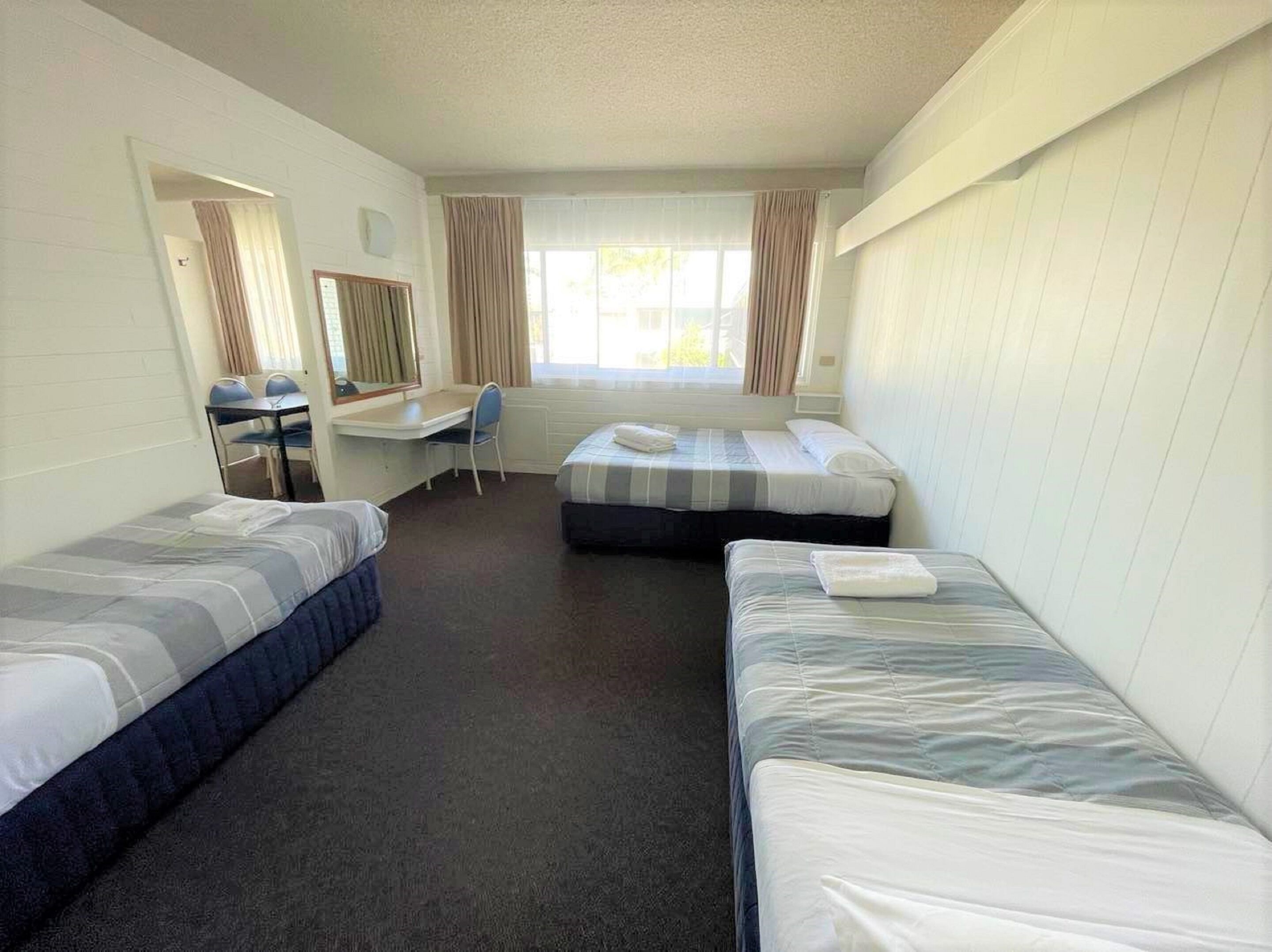 A hotel room with two single beds, a desk with a chair, a window with curtains, and a mirror.