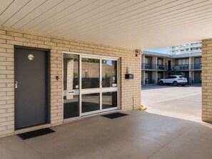 A building entrance with a dark door, a glass door, and a parking area with a white car.