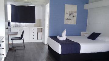 A modern hotel room with a bed, a desk, a chair, and a painting on the wall.